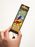 Hand holding a colourful Australian wildlife magnet and bookmark with black and gold detailing and an Australia-shaped charm against a warm white background.